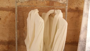 A bathroom with a metal towel rack holding two white towels. The wall is textured and has a rustic appearance.