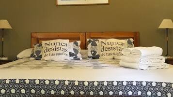 Un dormitorio con techo de madera, una cama con ropa de cama estampada, dos lámparas de noche y un cuadro en la pared.