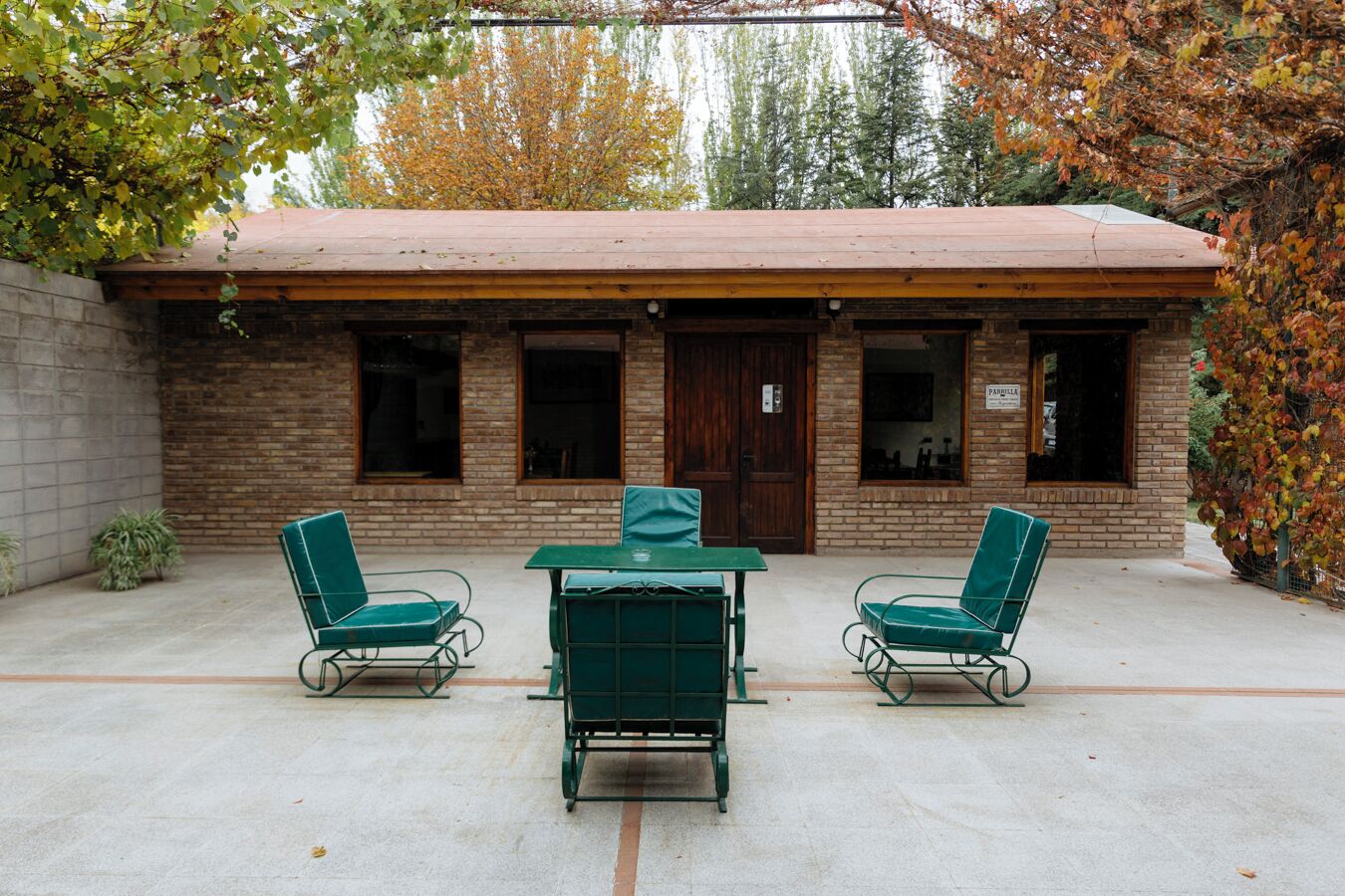 A building with a brick facade, a wooden roof, and a small patio area with two green metal chairs and a table.