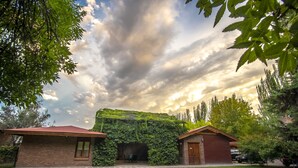 A brick house with a red roof, surrounded by a well-maintained lawn and trees. - Lujan de Cuyo B&B (Luján de Cuyo)