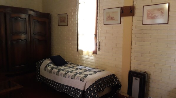 Une chambre avec un lit, une armoire, un radiateur et une fenêtre avec des rideaux.