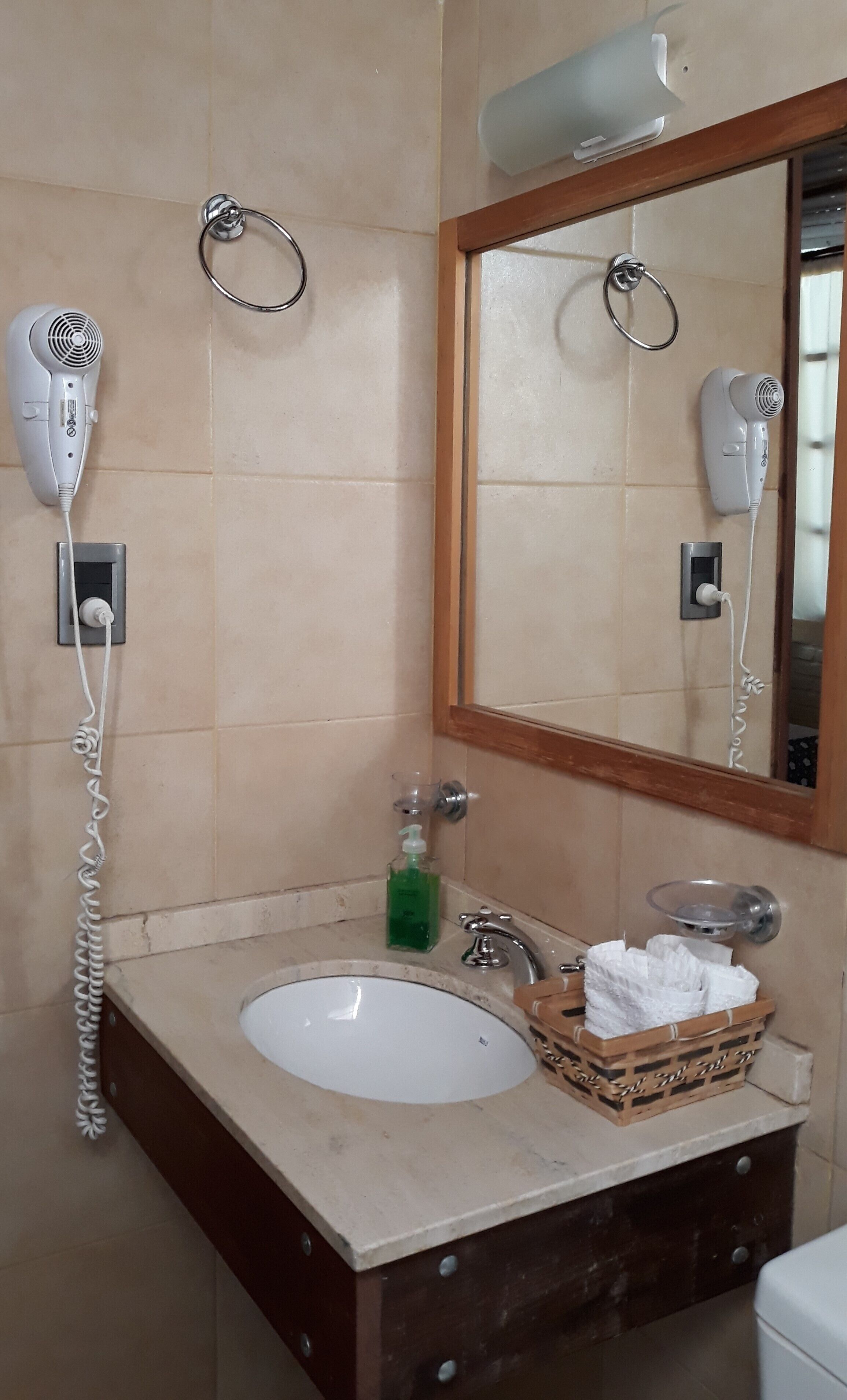 Un baño con lavamanos, espejo, secador de pelo y toallero.