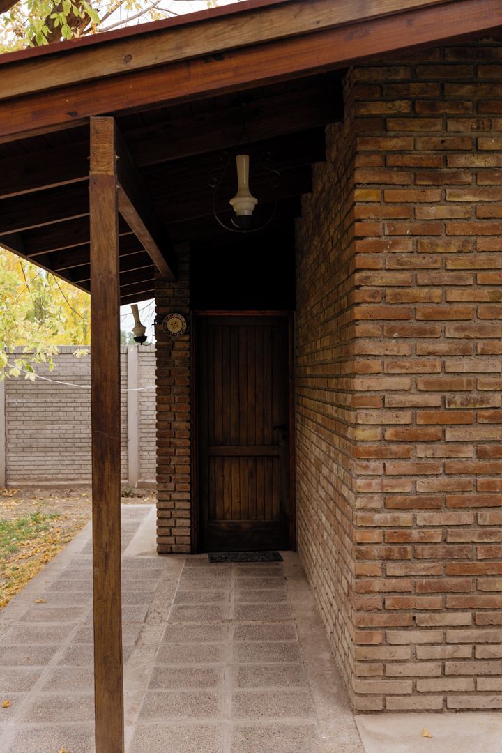 A covered outdoor area with a brick wall, a wooden door, and a ceiling fan.