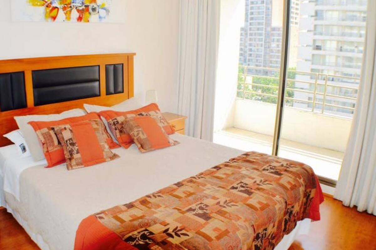 Une chambre d’hôtel avec un grand lit, une tête de lit en bois et une vue sur les gratte-ciel par la fenêtre.
