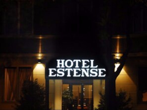 A hotel sign with the name "HOTEL ESTENSE" illuminated at night.