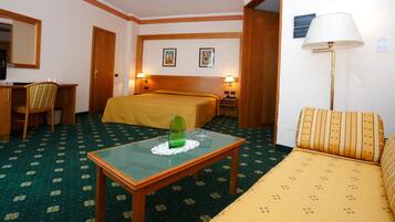 Ein Hotelzimmer mit Bett, Sofa, Schreibtisch mit Stuhl, Tisch mit Glasplatte und zwei Wandleuchten.