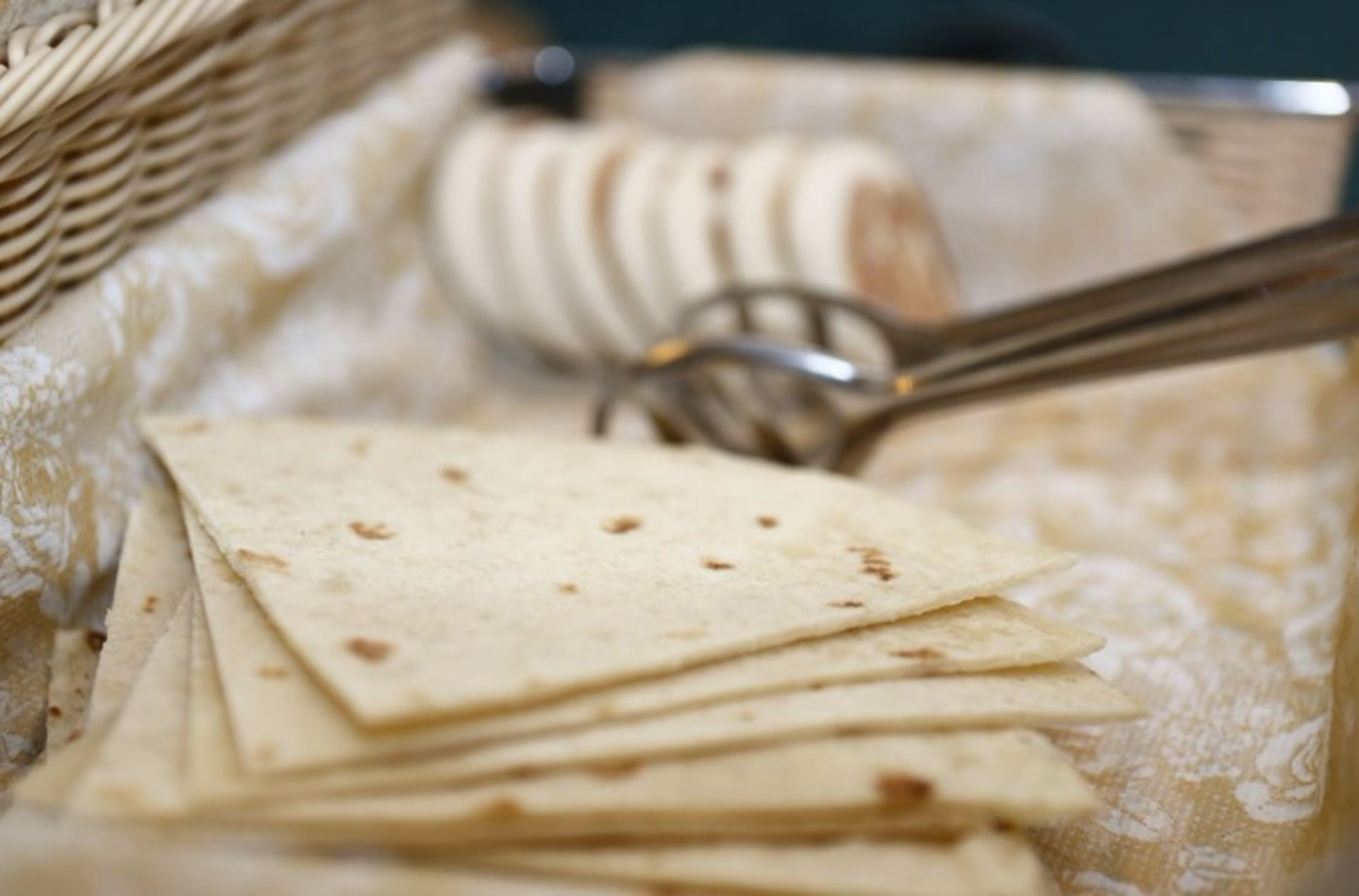 A stack of tortillas on a table with a fork and a basket in the background.