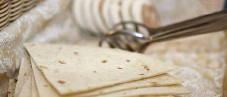 A stack of tortillas on a table with a fork and a basket in the background.