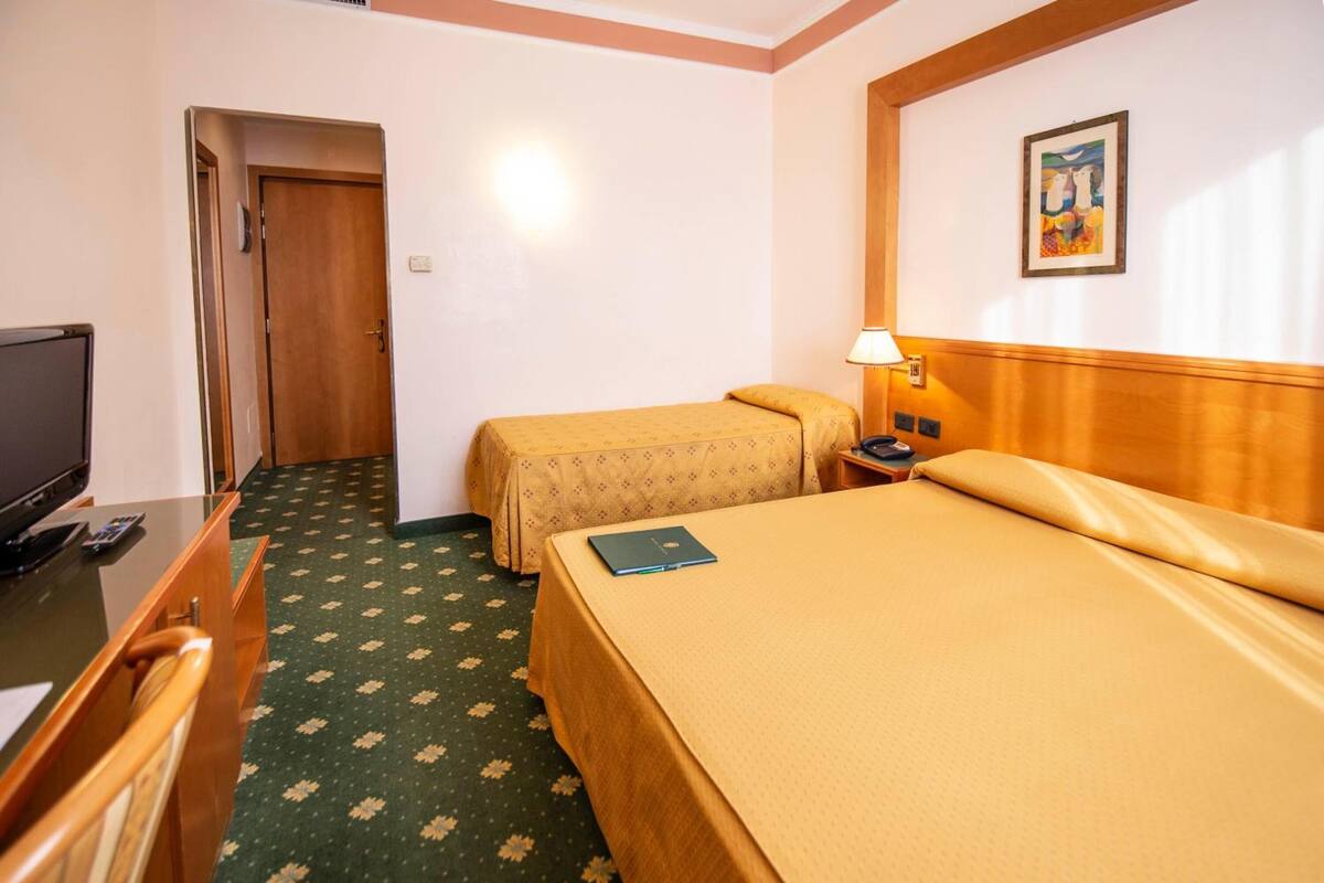 A hotel room with two beds, a desk with a computer, a lamp, and a painting on the wall.