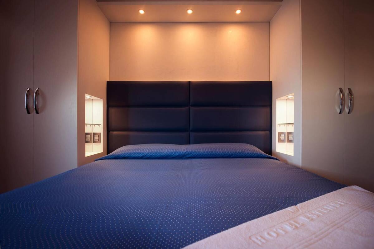 A modern hotel room with a large bed, padded headboard, bedside lamps, and a neutral color scheme.