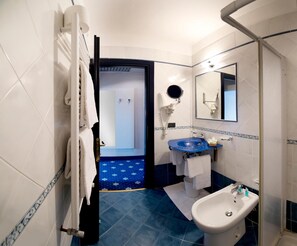 A bathroom with a blue patterned floor, a white sink with a blue basin, a white bidet, and a mirror above the sink.