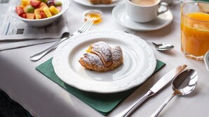 Une table de petit-déjeuner avec un croissant, un panier de fruits, du café et du jus d’orange.