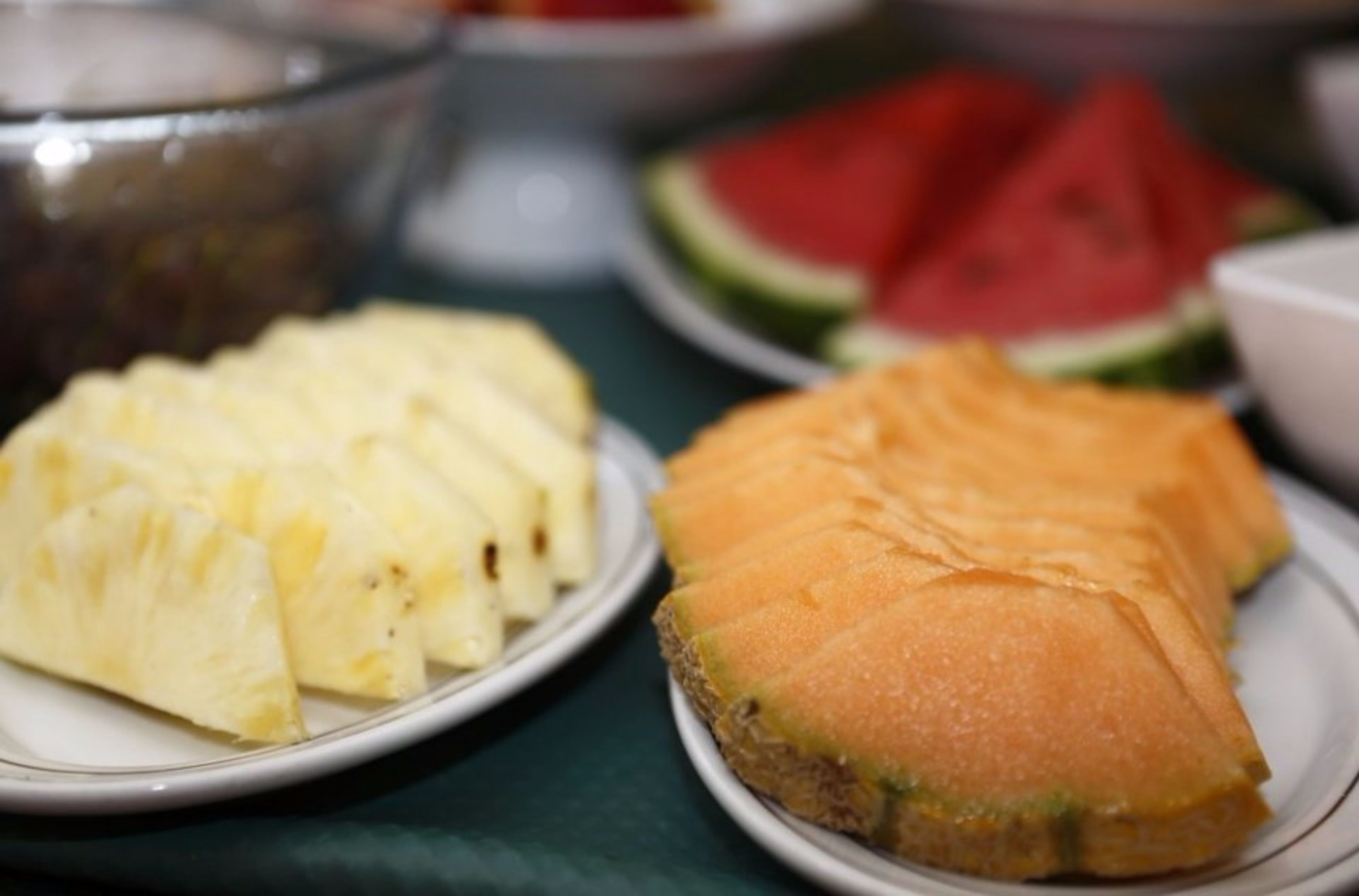 A table with plates of sliced pineapple and cantaloupe.