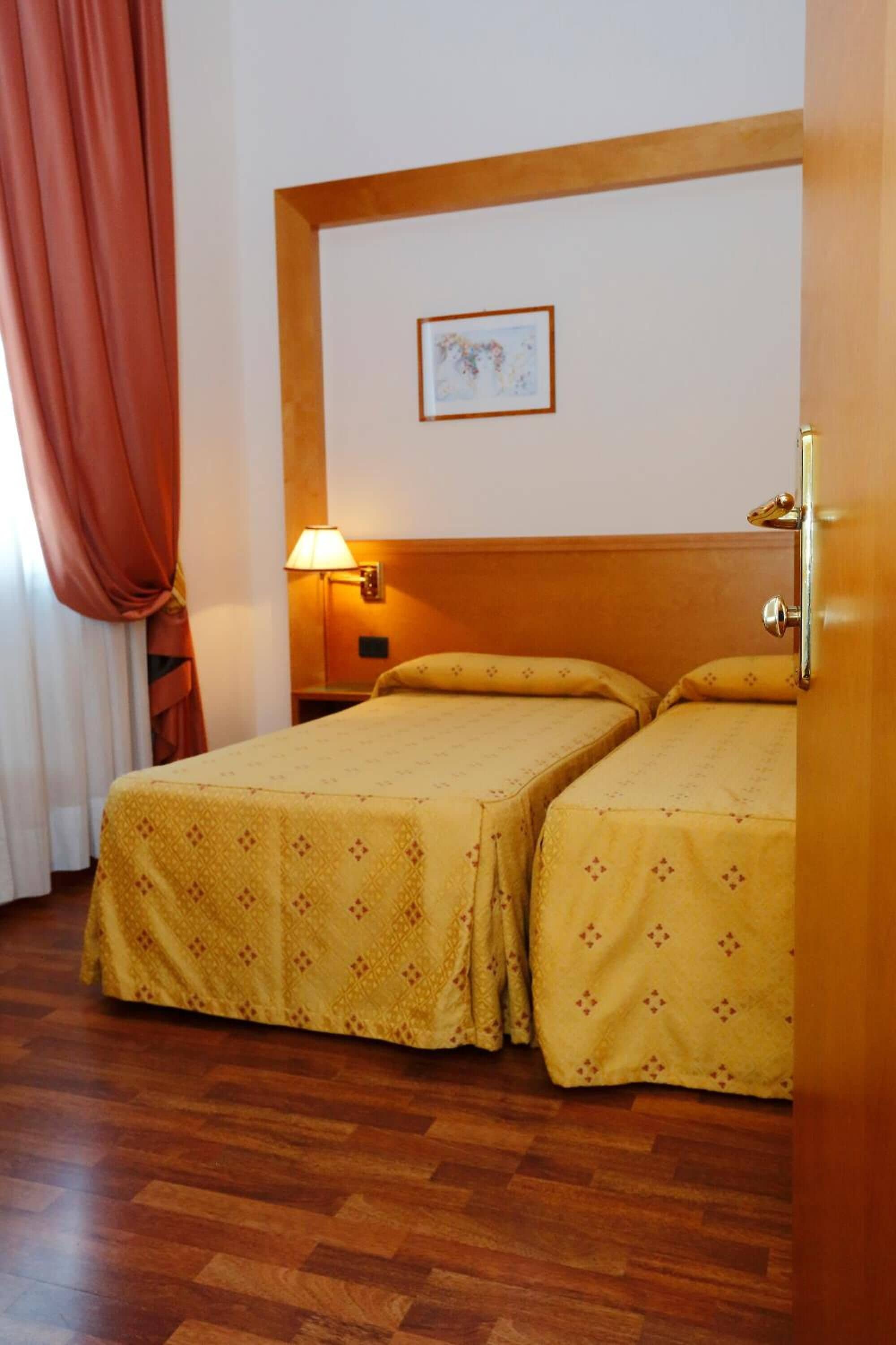 Une chambre d’hôtel avec deux lits, une tête de lit en bois, une table de chevet avec une lampe et un tableau encadré au mur.