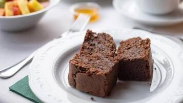 Un desayuno con una fuente de brownies, un bol de fruta y una taza de café sobre una mesa.