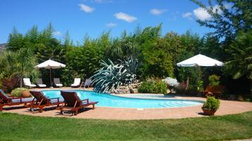 Una piscina al aire libre, sombrillas, sillones reclinables de piscina