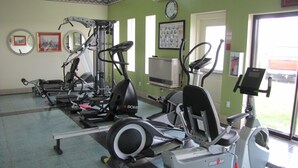Un gimnasio con diversas máquinas de ejercicio, un reloj y una ventana que ofrece vistas al exterior.