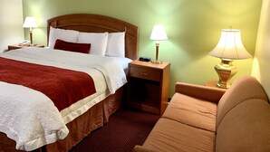 Habitación de hotel con una cama grande, dos mesitas de noche con lámparas, una mesita auxiliar, una silla y un cuadro en la pared.