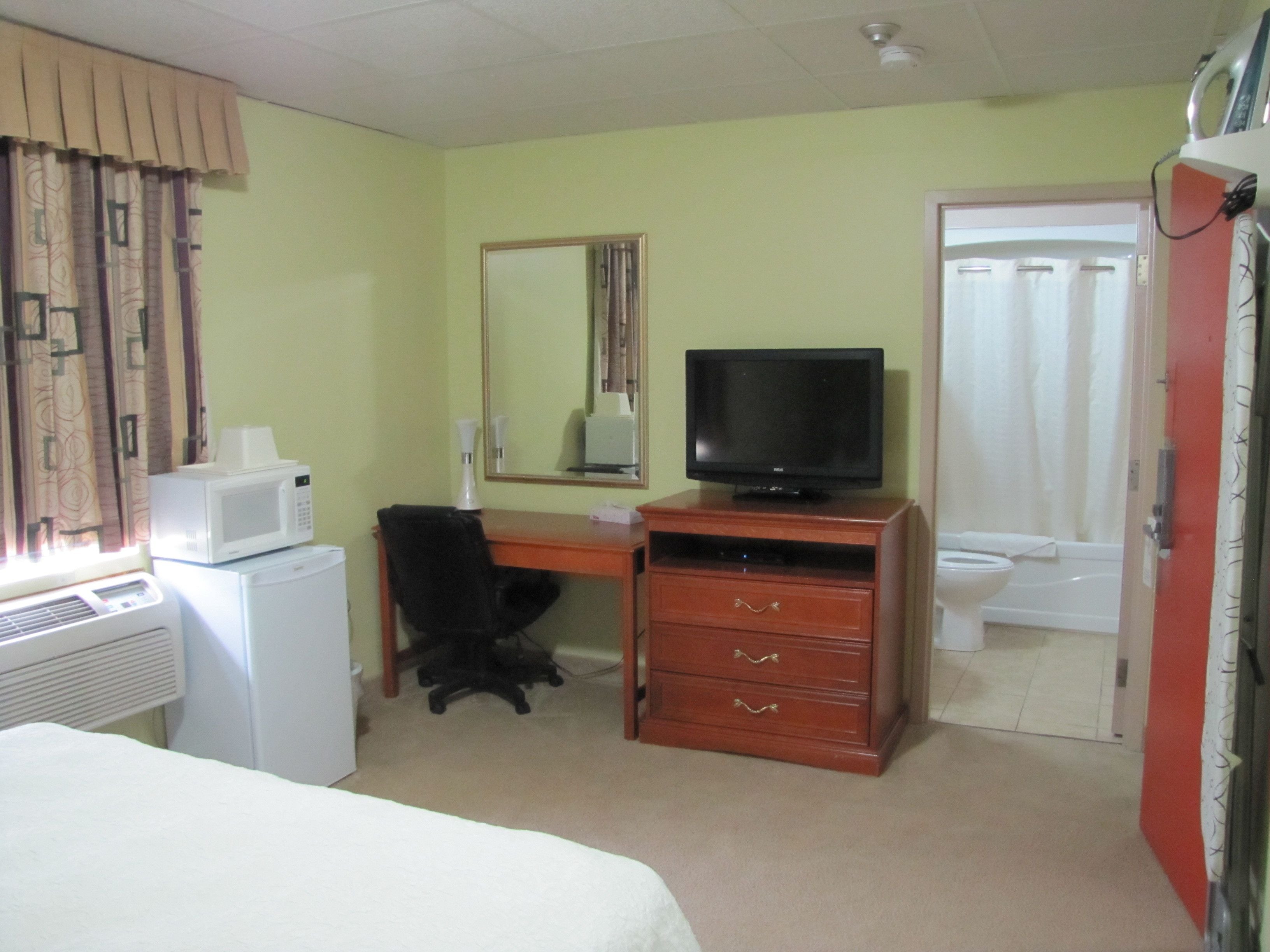 Habitación de hotel con cama, escritorio con computadora, televisor, microondas y baño con inodoro y ducha.