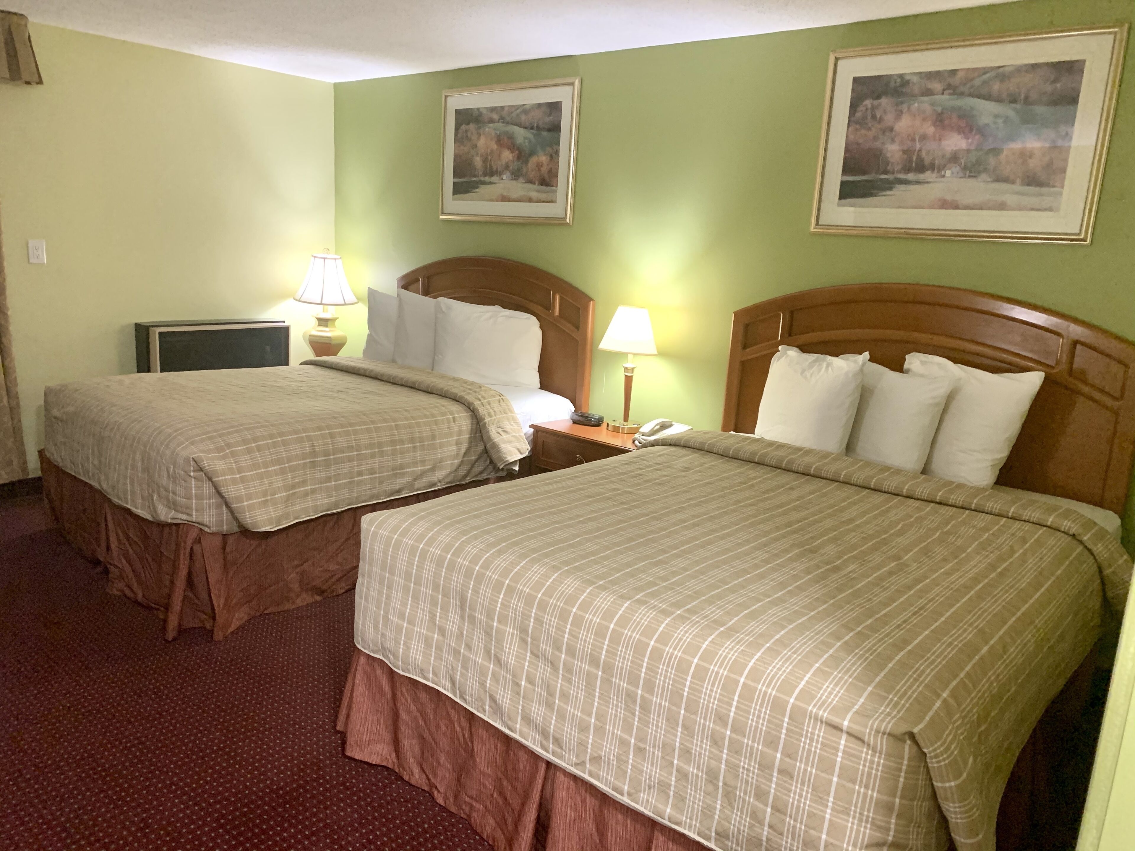 A hotel room with two beds, each with a wooden headboard, a nightstand with a lamp, and a wall-mounted TV.