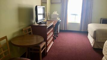 A hotel room with a bed, a desk with a computer, a chair, a round table, and a window with curtains.