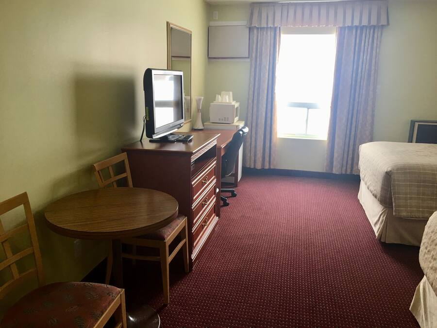 A hotel room with a bed, a desk with a computer, a chair, a round table, and a window with curtains.