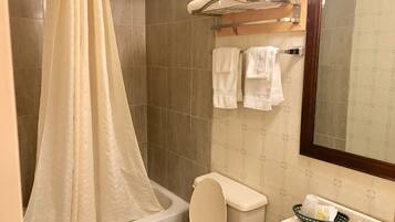 A bathroom with a shower curtain, a toilet, a sink with a mirror, and towels on a rack.
