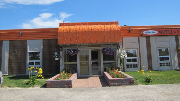 Un motel con entrada de ladrillo, jardines de flores y un letrero que dice "Valley Inn Motel & Suites".