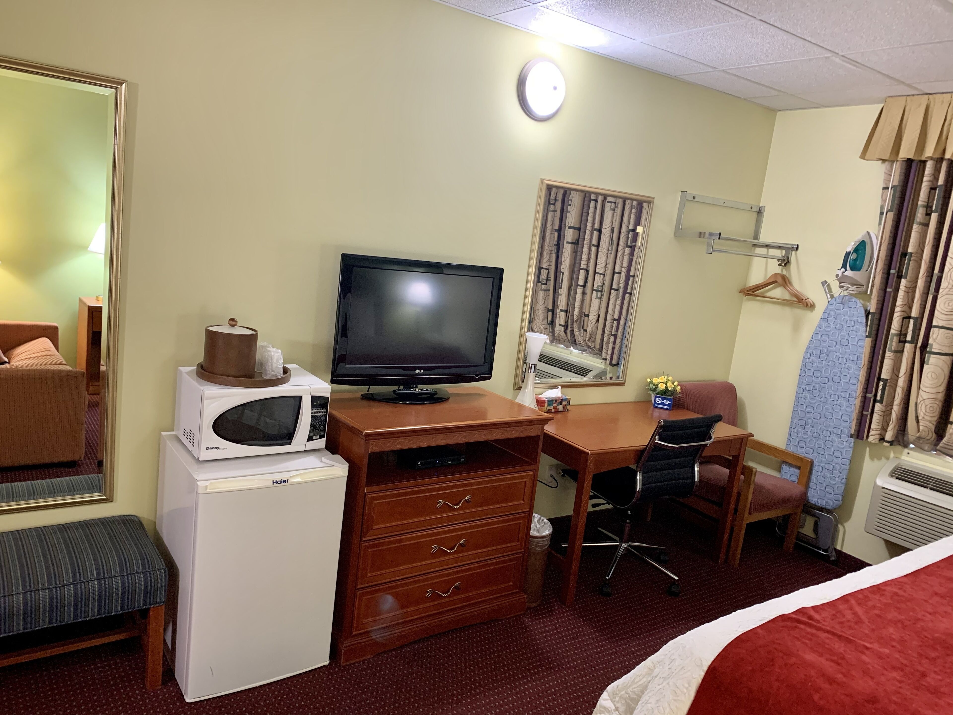 A hotel room with a bed, a desk with a computer, a television, a microwave, a heater, a chair, and a dresser.