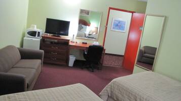A hotel room with a bed, a desk with a computer, a chair, a microwave, and a mirror.