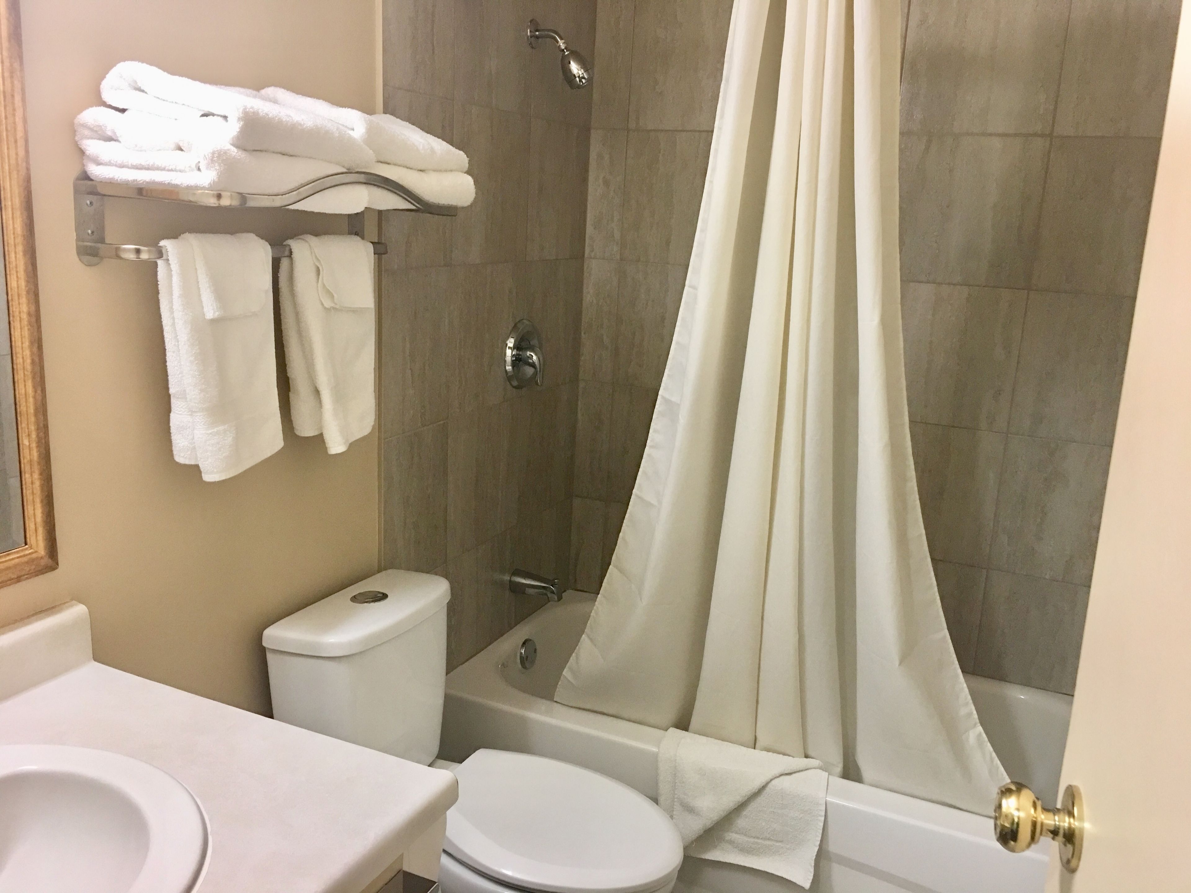 Un baño con inodoro, lavamanos y bañera. Hay toallas en un perchero y una cortina de ducha.