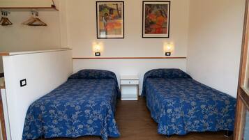 Een kamer met twee bedden, houten vloeren, een witte nachtkastje en twee wandlampen.
