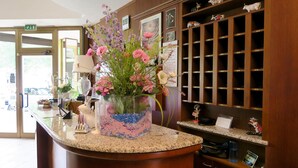 A reception area with a counter, a vase of flowers, and a wooden shelving unit with figurines.