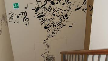 A staircase with a wall mural of musical notes and symbols, a green directional sign, and a window with blinds.