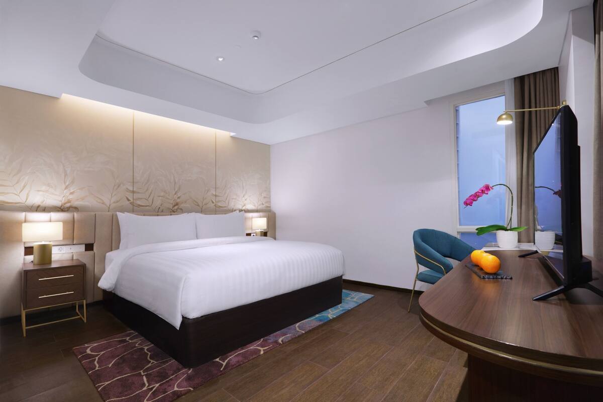 Een moderne hotelkamer met een groot bed, nachtkastjes, een bureau met stoel, een televisie en een raam met gordijnen.