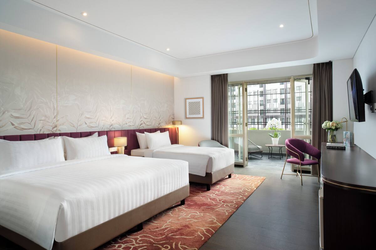 Hotelkamer met twee bedden, een bureau, een stoel, een televisie en een balkon met uitzicht.