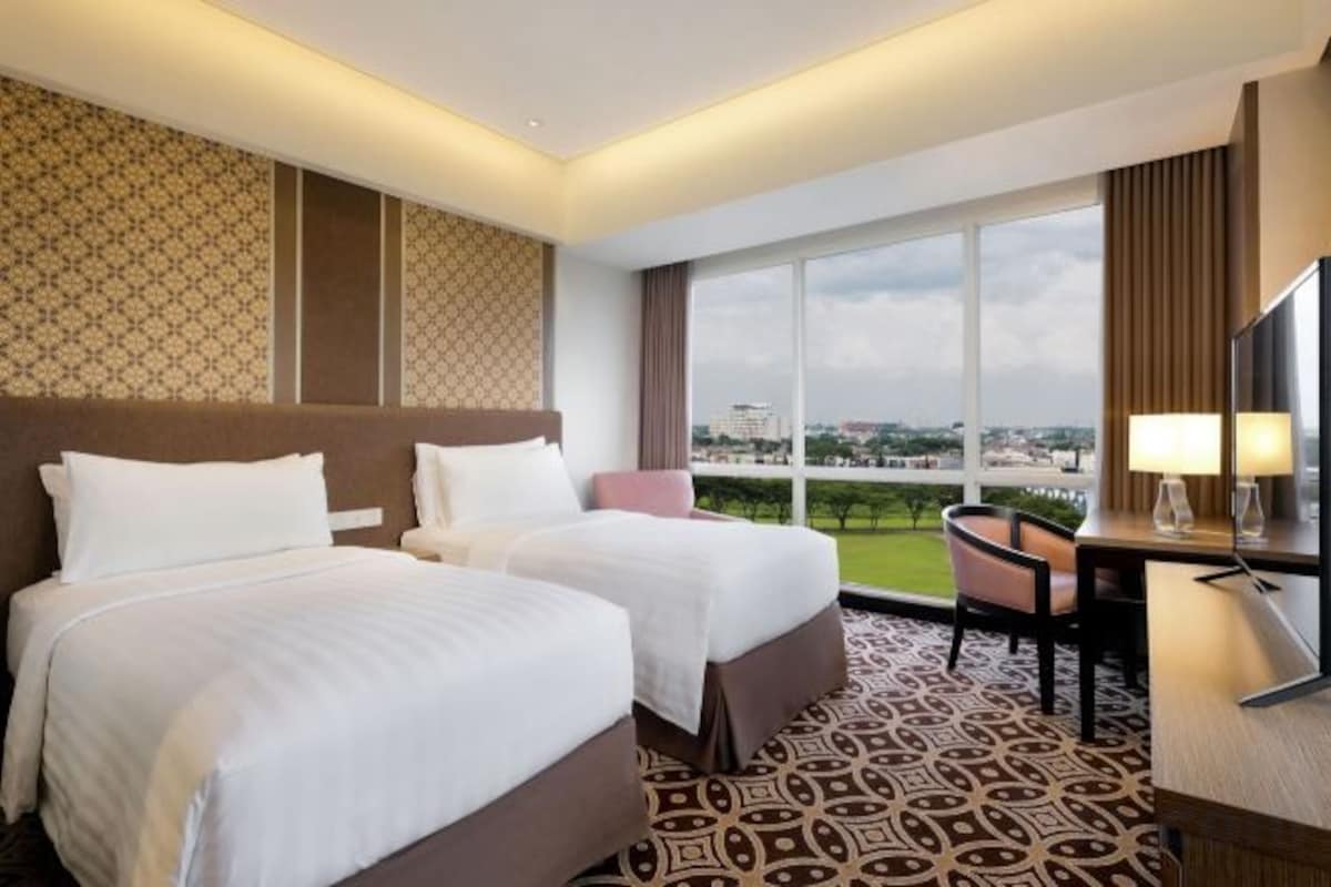 A hotel room with two beds, a desk, a chair, and a large window with a view.