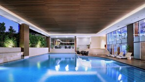 An indoor swimming pool with a wooden ceiling, glass walls, and a view of the outdoors. - Atria Hotel Gading Serpong (Gading Serpong)