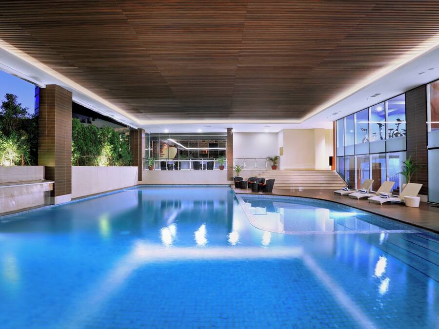 Una piscina interior con techo de madera, paredes de vidrio y vistas al exterior.