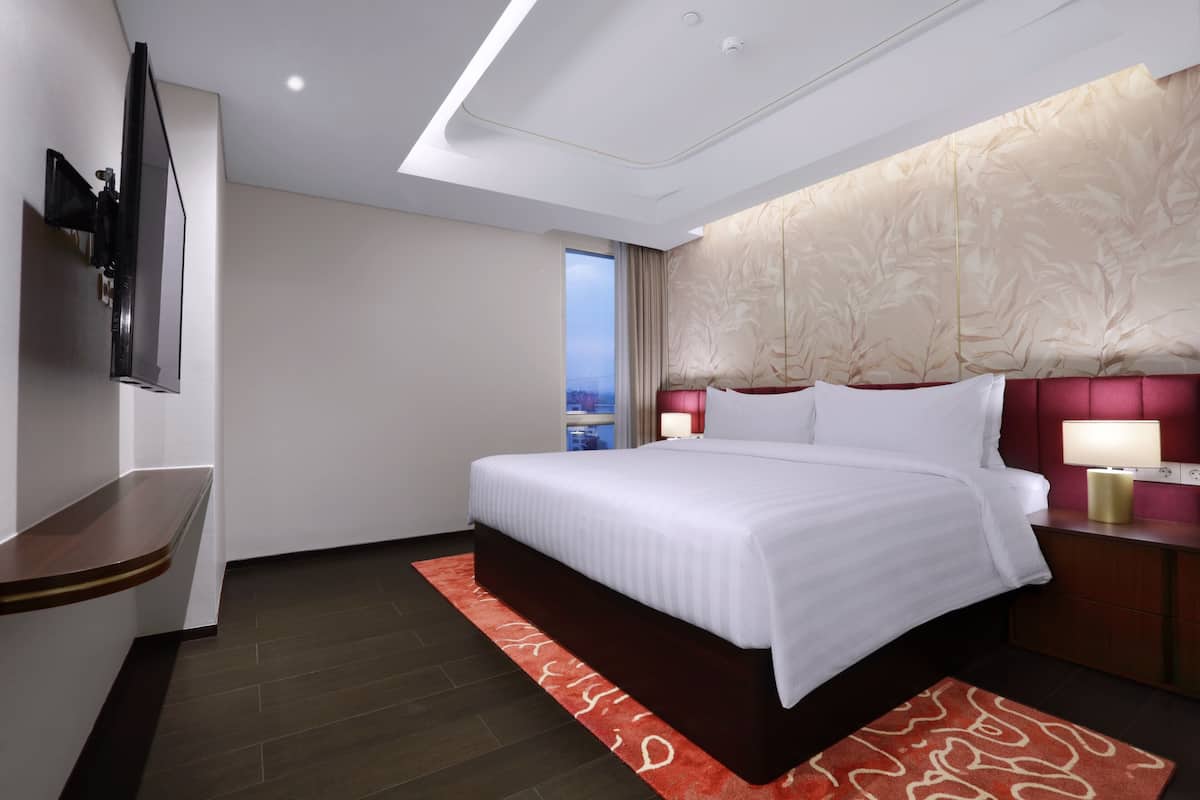 Een moderne hotelkamer met een groot bed, een aan de muur bevestigde televisie, een nachtkastje met een lamp en uitzicht op de stad.