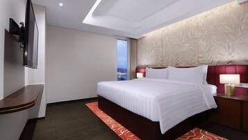 A modern hotel room with a large bed, a TV mounted on the wall, a nightstand with a lamp, and a view of the city through the window.