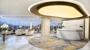 A modern hotel lobby with a reception desk, seating area, and large windows offering a view. - Atria Hotel Gading Serpong (Gading Serpong)