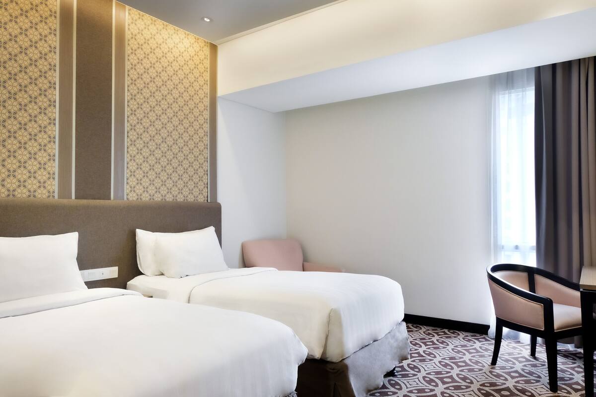 Een hotelkamer met twee bedden, een klein bureau, een stoel en een kamerbreed tapijt met een patroon.