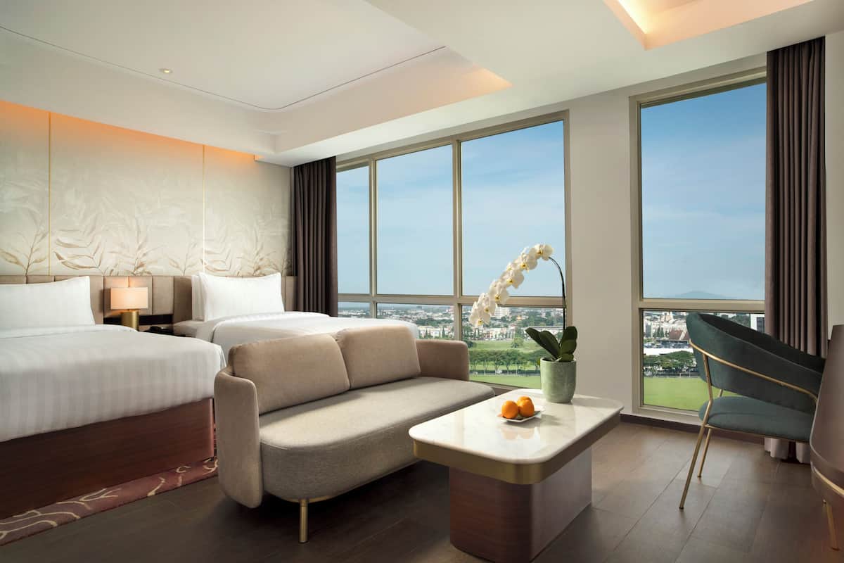 Hotelkamer met bed, sofa, bureau en grote ramen met uitzicht op de stad.