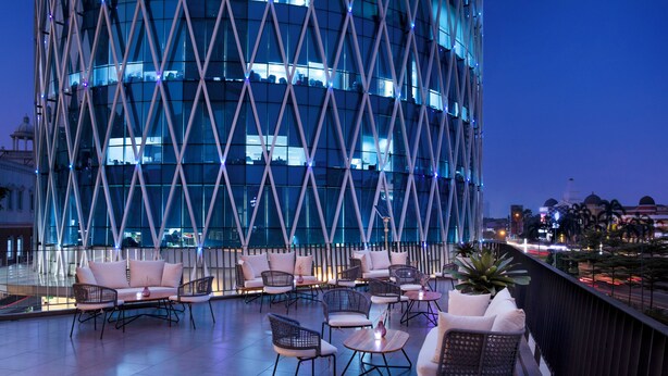 A rooftop terrace with outdoor seating, a modern building in the background, and a view of the cityscape. - Atria Hotel Gading Serpong (Gading Serpong)