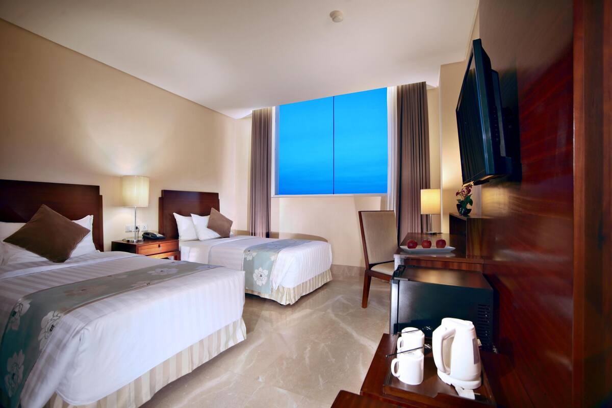 A hotel room with two beds, a desk with a telephone, a coffee maker, and a television.