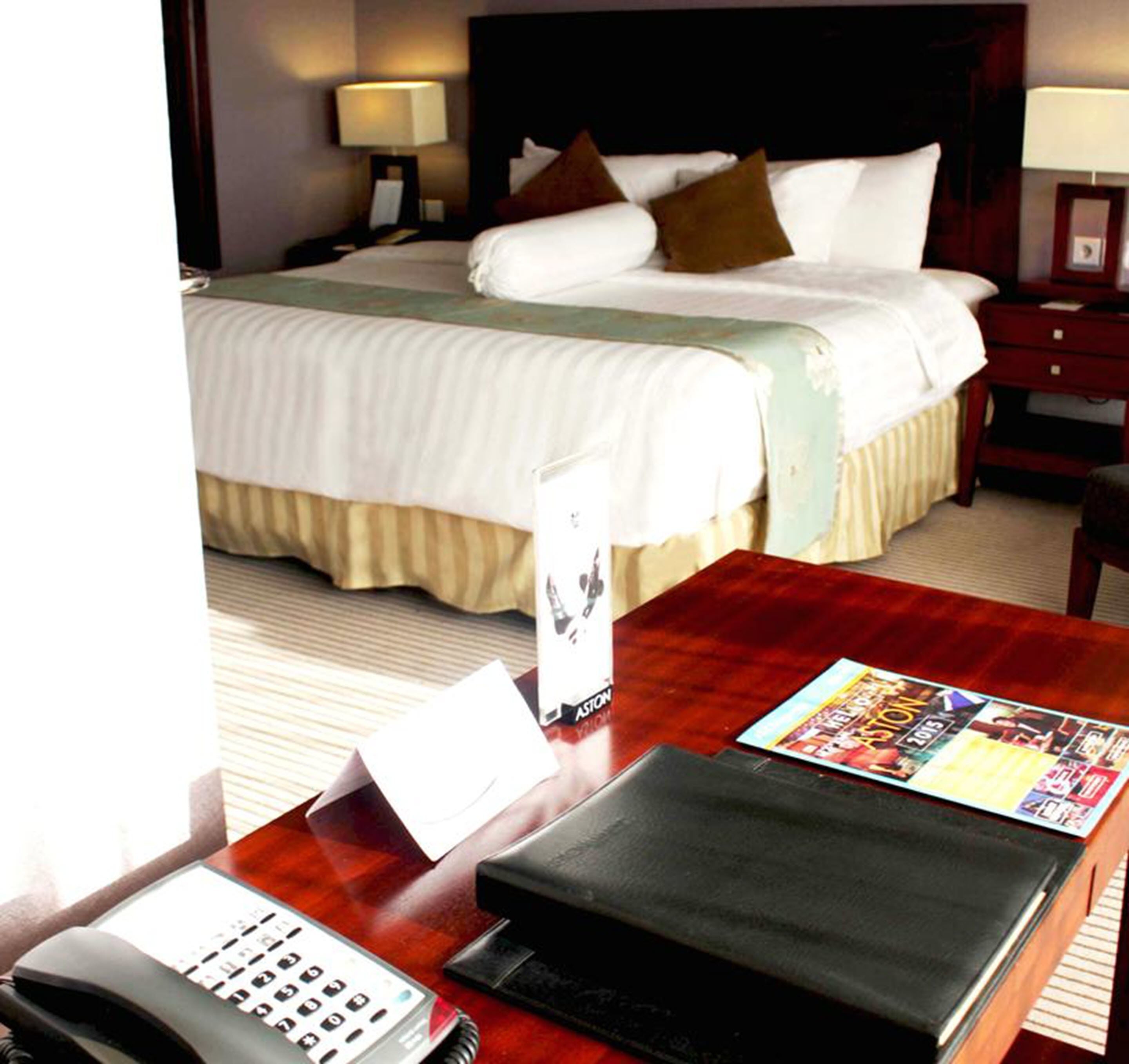 A hotel room with a bed, bedside tables, a desk with a telephone, and a magazine.
