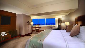 Een hotelkamer met een groot bed, een bureau, een televisie en uitzicht op de stad 's nachts.