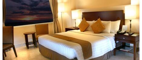 A hotel room with a large bed, two bedside tables, a chair, and a view of a sunset.