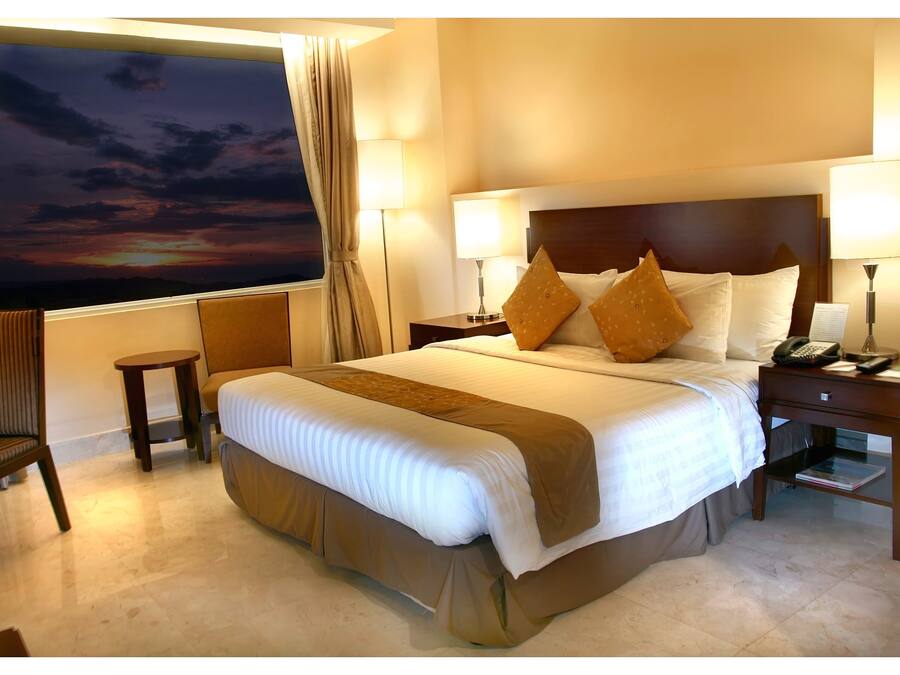 A hotel room with a large bed, two bedside tables, a chair, and a view of a sunset.
